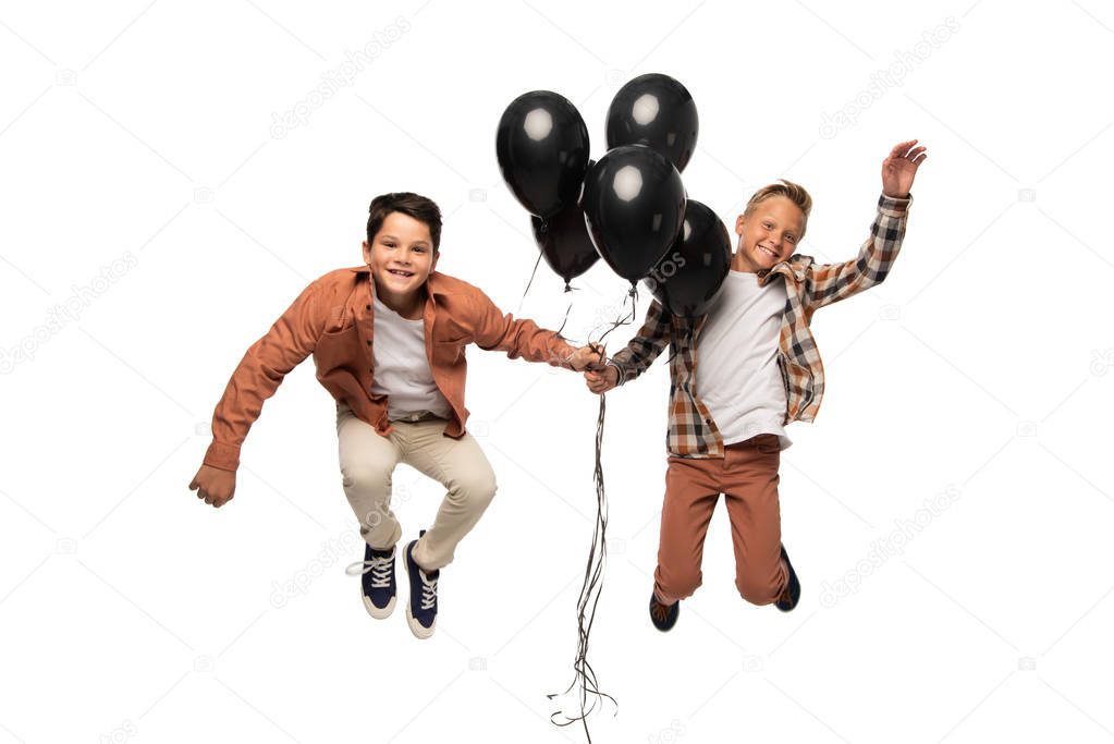 two happy boys levitating with black festive balloons isolated on white