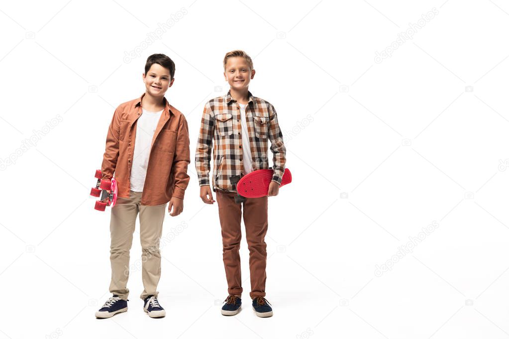 two smiling brothers holding penny poards and looking at camera on white background