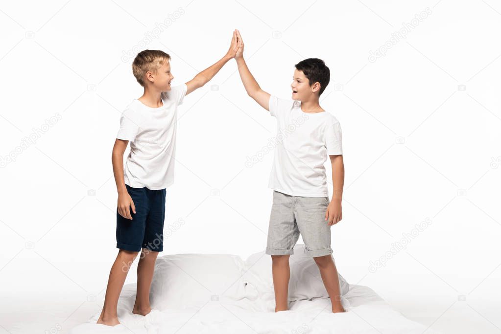two happy brothers standing on bed and giving high five isolated on white