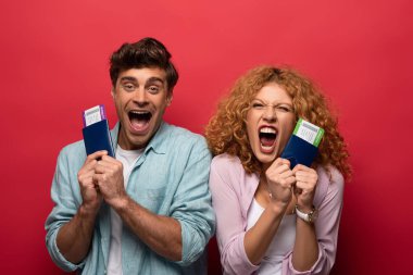 couple of excited travelers screaming and holding passports with air tickets, isolated on red clipart