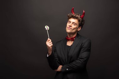 Cadılar bayramı şeytanı kostümlü yakışıklı adam elinde siyah bir lolipop tutuyor.