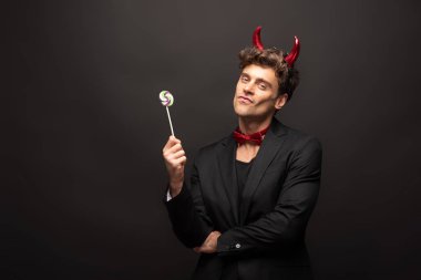 handsome man in halloween devil costume holding one lollipop on black clipart