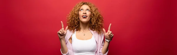 Atractiva Mujer Pelirroja Sorprendida Apuntando Hacia Arriba Aislado Rojo — Foto de Stock