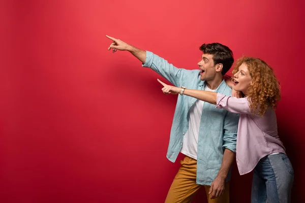 Belo Casal Animado Roupas Casuais Apontando Isolado Vermelho — Fotografia de Stock