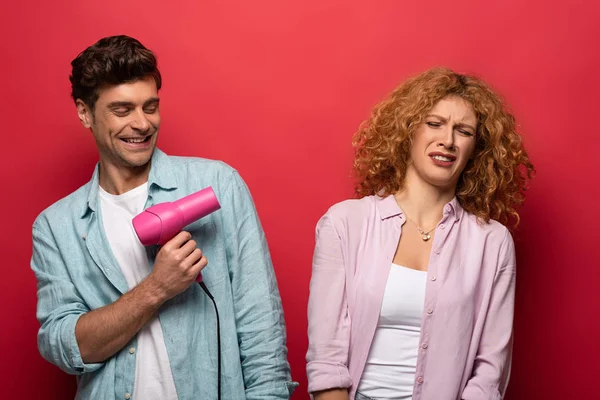 Belo Casal Divertindo Com Secador Cabelo Isolado Vermelho — Fotografia de Stock