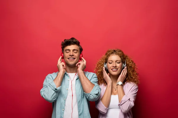Ευτυχισμένο Ζευγάρι Στα Ακουστικά Ακούγοντας Μουσική Κλειστά Μάτια Απομονωμένο Κόκκινο — Φωτογραφία Αρχείου