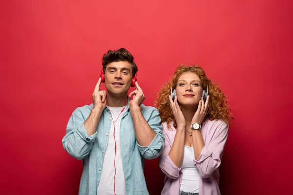 Hermosa Pareja Sonriente Escuchando Música Con Auriculares Juntos Aislados Rojo — Foto de Stock