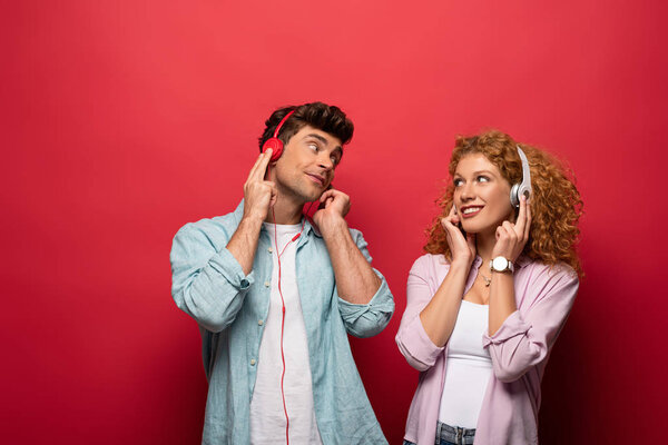 beautiful happy couple listening music with headphones and looking at each other, isolated on red