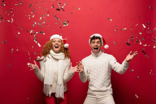 Excited Couple Santa Hats Screaming Celebrating Golden Confetti Isolated Red — Stock Photo, Image