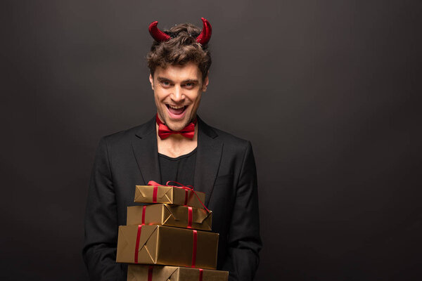 cheerful man in devil costume on halloween holding presents on black