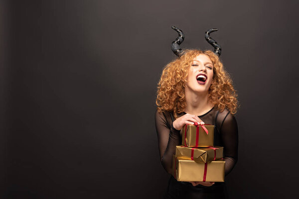laughing woman in maleficent costume holding presents for halloween on black