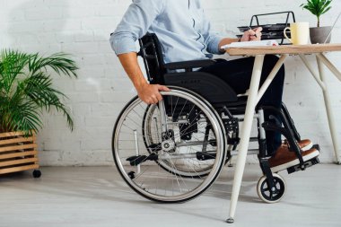 Tekerlekli sandalyedeki adamın iş yerindeki not defterine yazması.