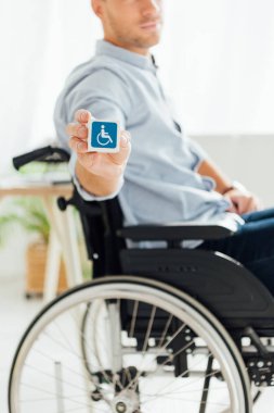 Tekerlekli sandalyedeki adam engelli işareti olan küpü gösteriyor. 