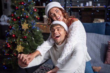 Noel Baba şapkalı gülümseyen erkek ve kız arkadaş Noel zamanı el ele tutuşuyorlar. 