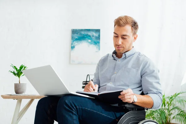 Mann Rollstuhl Schreibt Notizbuch Schreibtisch Mit Laptop — Stockfoto