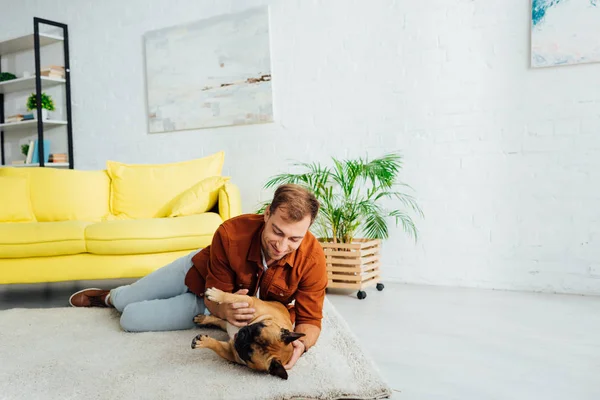 Leende Man Leker Med Fransk Bulldogg Golvet Vardagsrummet — Stockfoto