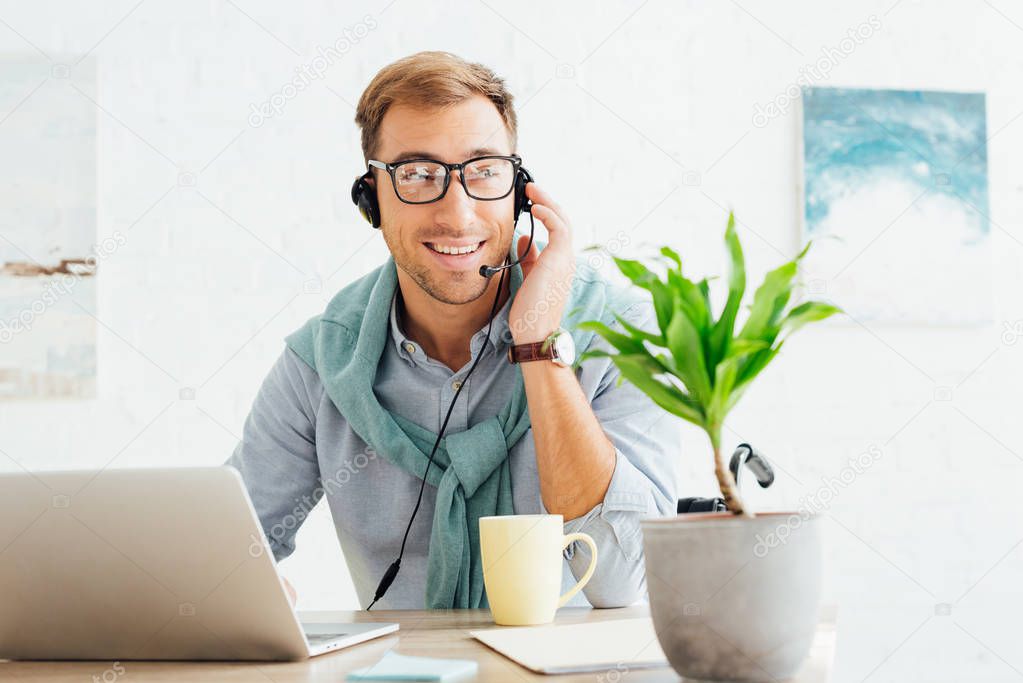 Smiling call center operator in wheelchair talking on headset at workplace