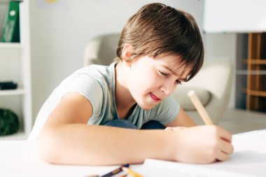 kid with dyslexia drawing with pencil and sitting at table  clipart
