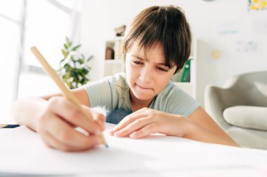 Kalemle resim çizen ve masada oturan disleksisi olan çocuk. 