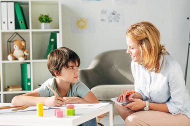 kid with dyslexia holding pencil and smiling child psychologist talking to him  clipart
