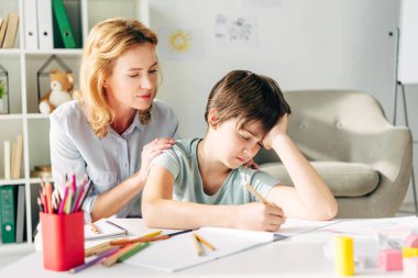 kid with dyslexia drawing with pencil and child psychologist looking at it  clipart