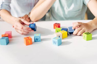 cropped view of child psychologist and kid with dyslexia playing with building blocks clipart