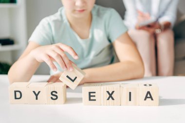 cropped view of kid with dyslexia sitting at table and playing with wooden cubes clipart