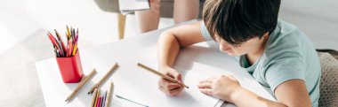 panoramic shot of kid with dyslexia drawing on paper with pencil  clipart