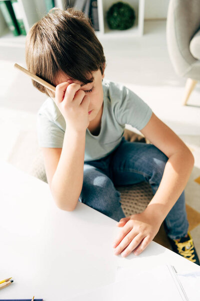 high angle view of sad kid with dyslexia holding pencil 
