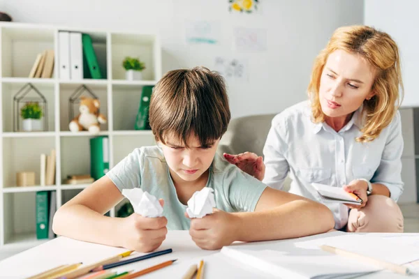 Rozdrażniony Dzieciak Dysleksją Trzymający Pogniecione Papiery Psycholog Dziecięcy Rozmawiający Nim — Zdjęcie stockowe