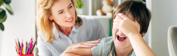 Πανοραμική Λήψη Του Παιδιού Δυσλεξία Συσκοτίζοντας Πρόσωπο Και Χαμογελαστός Παιδοψυχολόγος — Φωτογραφία Αρχείου