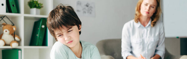 Панорамный снимок грустного ребенка с дислексией и детским психологом, смотрящего на него
 
