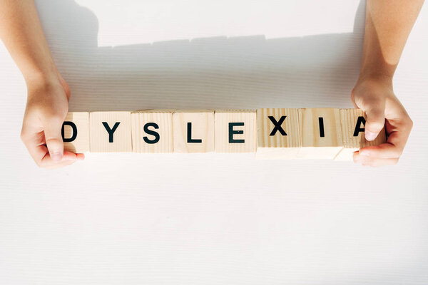 обрезанный вид ребенка с дислексией держа деревянные кубики с надписью
 
