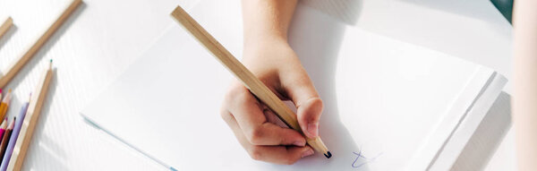 cropped view of kid with dyslexia drawing on paper with pencil 