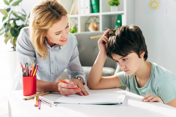 Dziecko Dysleksją Uśmiechniętym Psychologiem Siedzącym Przy Stole Trzymającym Ołówki — Zdjęcie stockowe