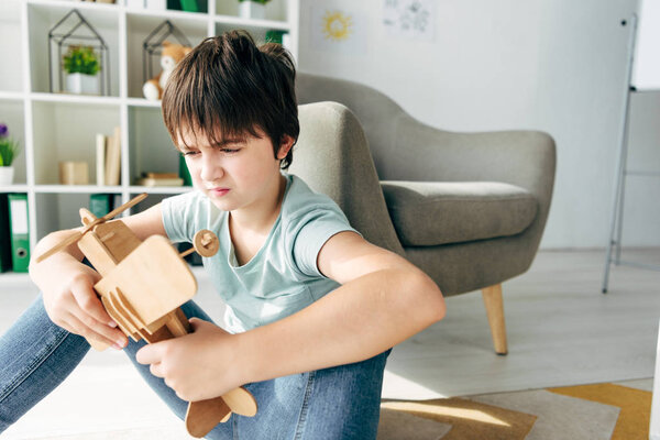 sad kid in t-shirt with dyslexia holding wooden plane 