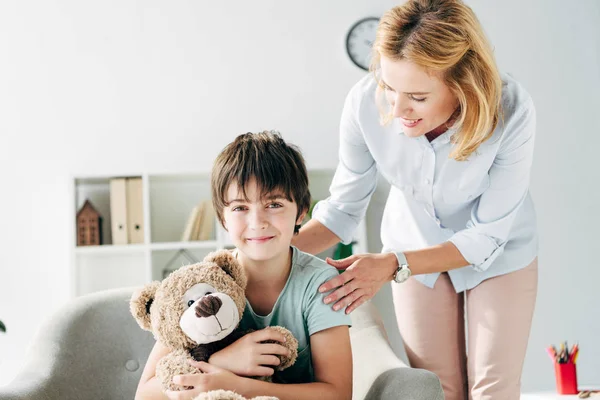 Niño Sonriente Con Dislexia Sosteniendo Oso Peluche Psicólogo Infantil Mirándolo — Foto de Stock