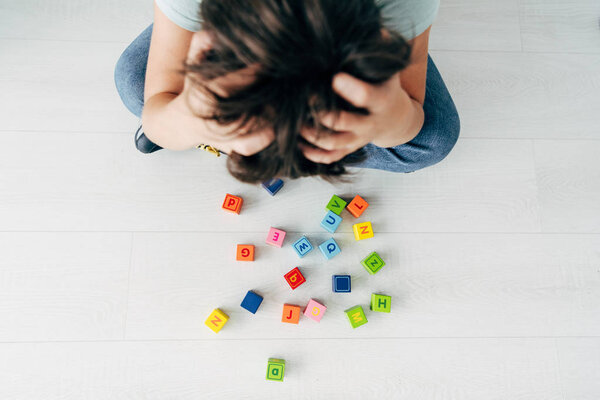 top view of sad kid with dyslexia sitting near building blocks