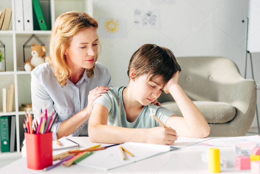 kid with dyslexia drawing with pencil and child psychologist looking at it 