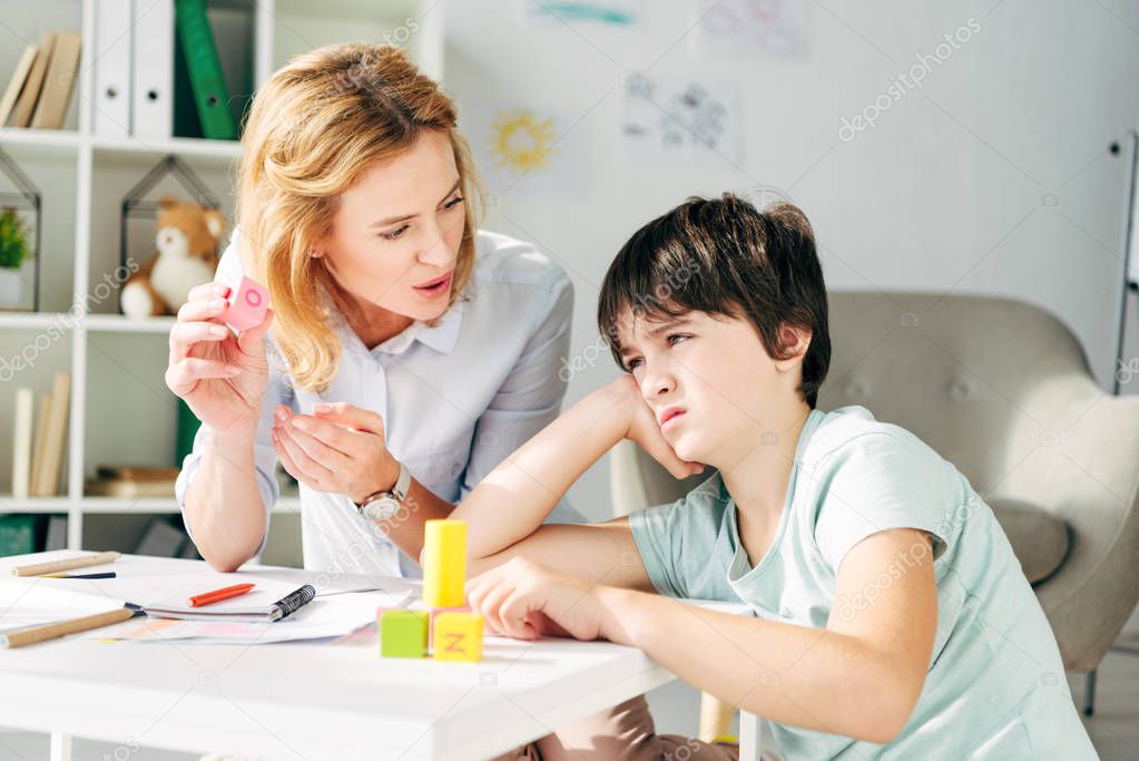 sad kid with dyslexia and child psychologist playing with building blocks