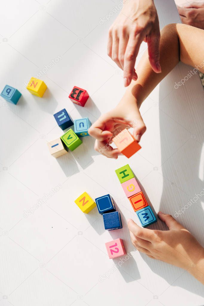 cropped view of child psychologist and kid with dyslexia playing with building blocks