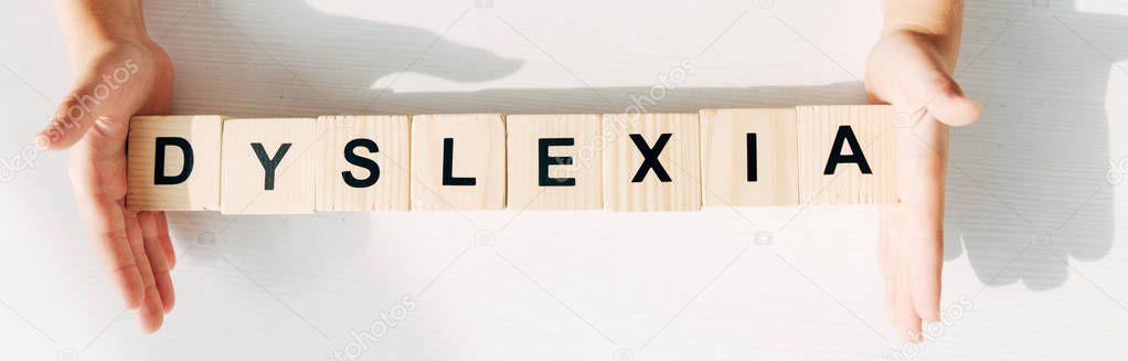 panoramic shot of kid with dyslexia holding wooden cubes with lettering 