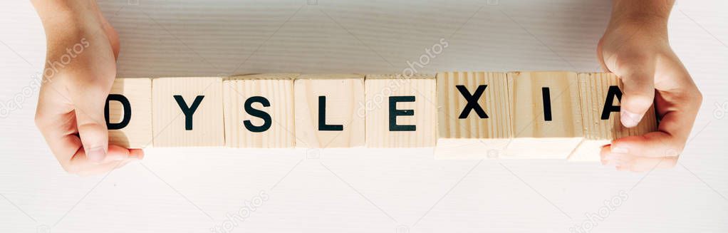 panoramic shot of kid holding wooden cubes with lettering dyslexia 