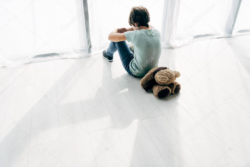 high angle view of kid with dyslexia sitting on floor with teddy bear 