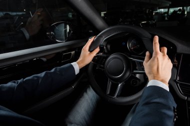 KYIV, UKRAINE - OCTOBER 7, 2019: cropped view of driver touching steering wheel while sitting in porshe  clipart