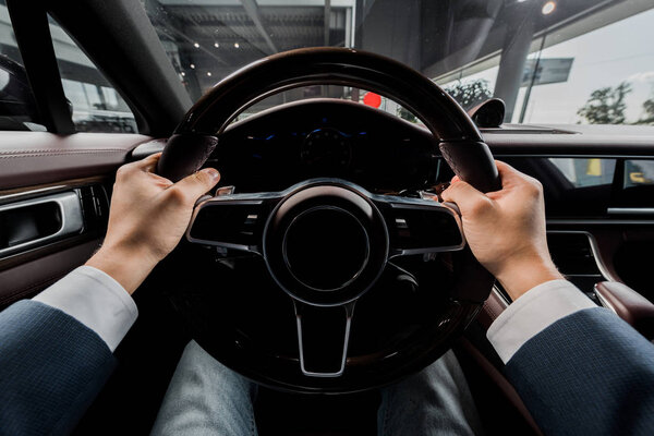 KYIV, UKRAINE - OCTOBER 7, 2019: cropped view of driver holding steering wheel while sitting in modern porshe