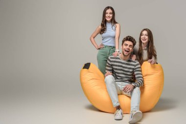 Neşeli arkadaşlar çöp tenekesinde birlikte oturuyorlar, gri sandalyede.