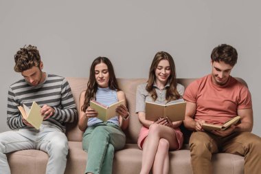 Genç arkadaşlar gri kanepede otururken kitap okuyorlar.