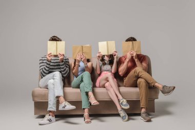 arkadaşlar kitap okurken gri kanepede oturuyorlar.