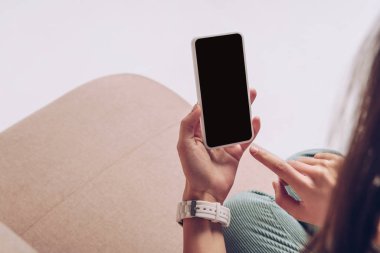 Gri kanepede izole bir şekilde otururken akıllı telefon kullanan bir kızın görüntüsü.